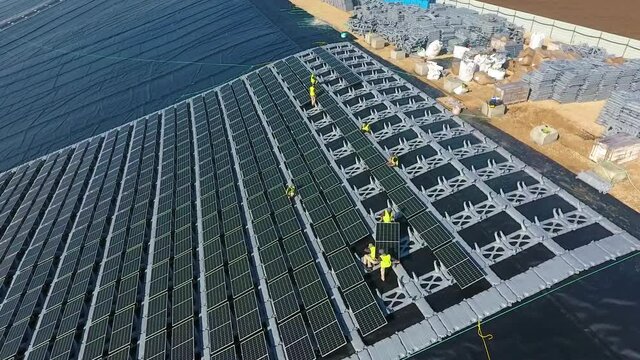 Slow aerial pullback over a solar array, showing workers in yellow manipulating components. Drone.