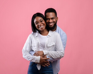 Portrait of lovely African American couple hugging and cuddling, feeling happy on pink background. Valentine's Day