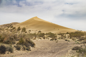 Fototapeta na wymiar Sand dune against the blue sky. Against the background of a cloudy sky, a sand dune in the desert, sunny summer day, the road in the sand