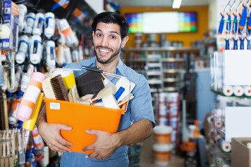 Happy male artisan with tools in hands satisfied with purchases in paint store