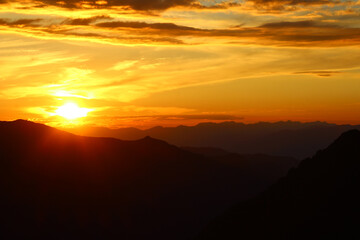 Yellow sunset with the sun in the mountains with the sun in the Kara-Turek pass, with silhouettes of mountains against, Altai, Belukha, the sky in summer. Sunset sky high in the mountains in the Altai