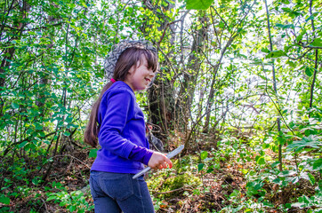 little girl picking mushrooms in the pine forest .