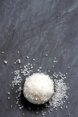 coarse white sea salt in a glass bowl is scattered on the table - top view. On a gray concrete background. copy space