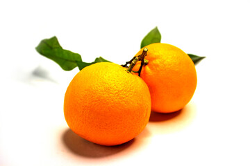Oranges. Ripe round fruits with green twigs and leaves. Textured orange peel. Close-up on a white background.