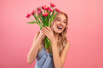 Happy Woman's Day. Excited young lady in cocktail dress holding bouquet of tulips on pink studio background