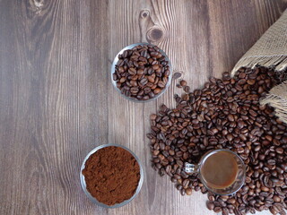 Robes of roasted coffee and intense toast in heaps, accompanied by bowl with ground coffee on a wooden table