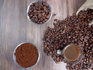 Robes of roasted coffee and intense toast in heaps, accompanied by bowl with ground coffee on a wooden table