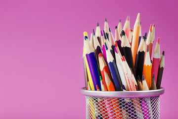 Pencils of different colors in a glass on a pink background.