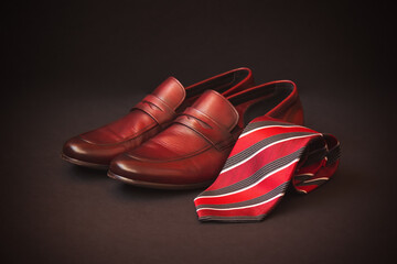 Red striped rolled necktie and brown men's shoes. Selective focus.