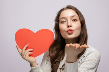 Young girl showing red heart from cardboard to camera and blows a kiss, valentine's day