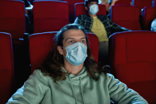 Young guy wearing protective face masks while watching movie in cinema auditorium during covid19 pandemic