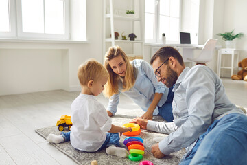Happy family. Mom, dad and baby playing at home with a colored pyramid sitting on the floor in the living room. Parents together develop their child. Concept of family and child development.