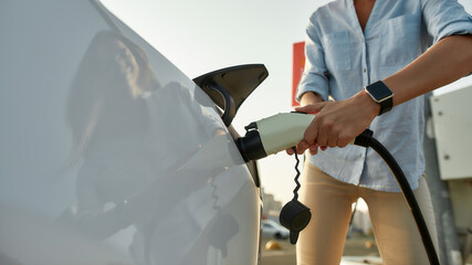 Woman plugging electricity cable in vehicle for charging