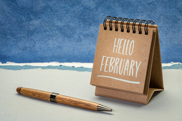 hello february greeting card - handwriting in a spiral desktop calendar against abstract paper landscape, calendar concept