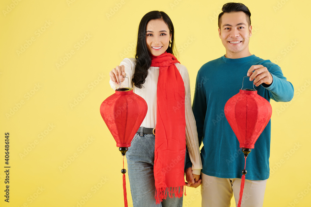 Sticker cheerful vietnamese boyfriend and girlfriend in winter sweaters holding hands and showing red paper 