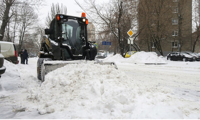 The tractor removes large snowdrifts from the road. Snow removal after heavy snowfall.