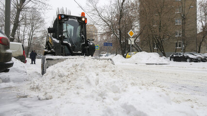 The tractor removes large snowdrifts from the road. Snow removal after heavy snowfall.
