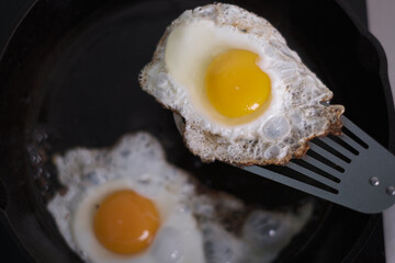 Two crispy fried eggs in a cast iron skillet, stainless steel spatula.