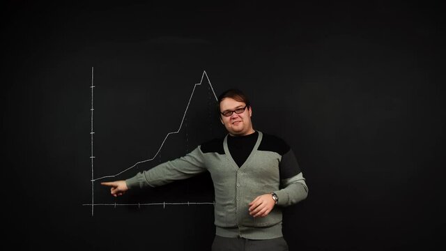 Man stands near blackboard and draws graphic with raising and falling level forming economic bubble. A trader explains stock prices development. Concept of business training. Theme of entrepreneurship