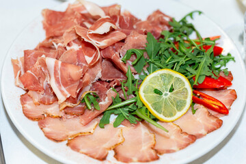 Sliced meat on a plate in a restaurant decorated with greens. Sausage, salami, lard, ham sliced on a plate