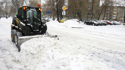 The tractor removes large snowdrifts from the road. Snow removal after heavy snowfall.