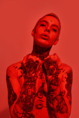 Tattoo and piercing. A close up of a white woman with tattoos and piercing standing topless looking into a camera with her hands covering breasts