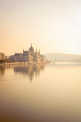 Fototapeta na wymiar Hungarian Parliament landscape in sunset light next to the Danube with boats with foggy air and Gellert hill in the background and the Chain bridge