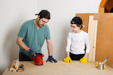 Father and son grind board or plywood with grinder. Teenager learns to work with grinder. Carpenter...