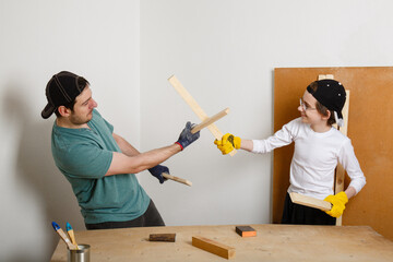 father and son spend time together in the workshop. Break from work for games. Comic fight with swords from wooden slats. Father's day. Family fun concept. DIY at home. New normal. Dad and teenager 