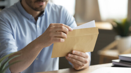 Close up young man opening envelope with paper correspondence. Curious businessman getting paper...
