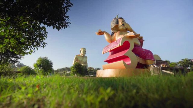 4k Pan towards Three headed Elephant. Foreground of green grass. golden monk statue Luang Pu Thuat at dawn. Big Buddha, Golden Statue in mountains at beautiful sunrise in Khao Yai. depth of field