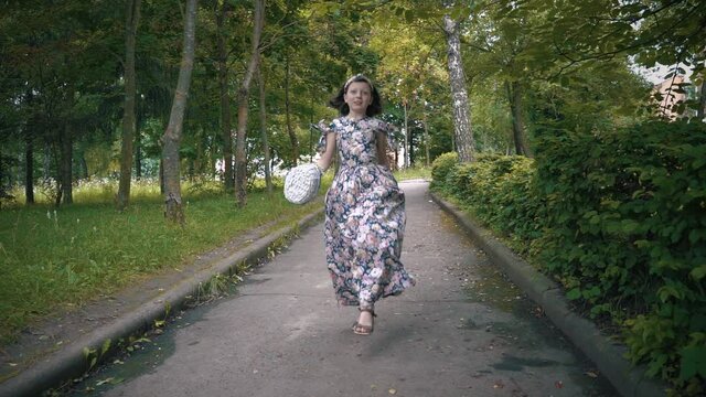 Cheerful and happy girl jumps on the path in the park with a basket of flowers in his hands