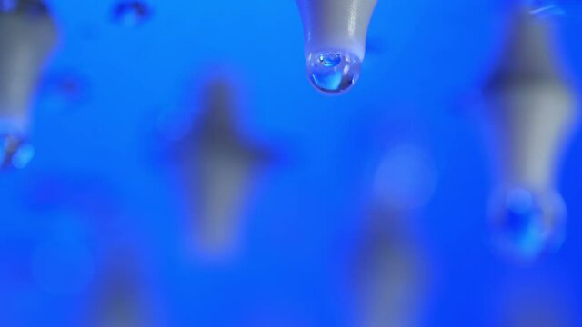 Macro shot of droplets of water dropping from a metallic shower tube.
