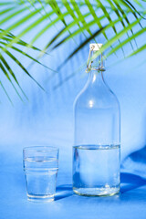 Glass with water near to bottle on blue background