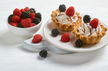 Two cakes on a light plate with blackberries and raspberries. Nearby is a bowl with berries.