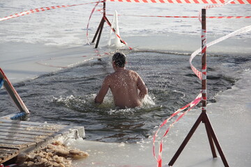 Winter ice swimming sport, a Caucasan man in a swimming trunks in the ice hole water on a Sunny...
