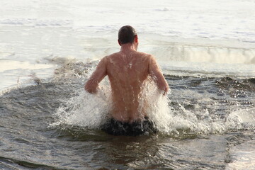 Winter ice swimming sport, a Russian man in a swimming trunks swimm in the ice hole water with splashes on a Sunny frosty winter day, healthy lifestyle