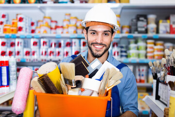 Cheerful smiling workman holding basket with picked tools in paint store