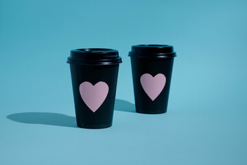 Two stacked black paper cups for hot drinks with pink hearts on