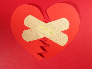 Red broken bandaged heart on red background.