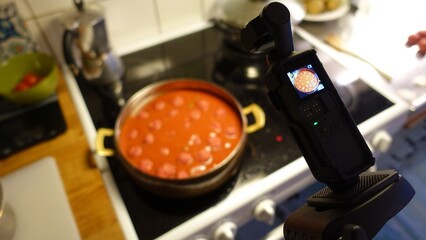 A digital camera is filming homemade meatballs simmering in tomato sauce