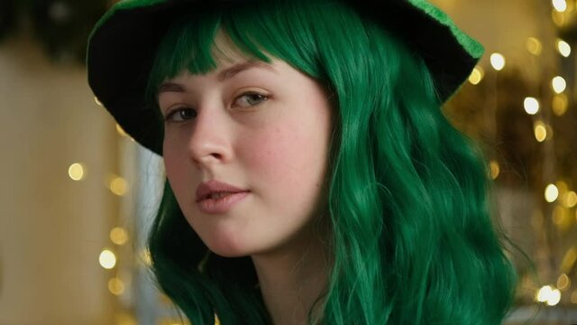 Saint Patrick's day party concept. Closeup portrait of beautiful caucasian teen girl with green hair and hat. Slow motion.
