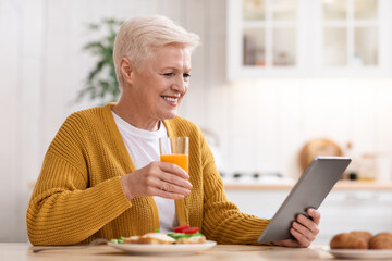 Joyful old woman eating healthy food and using digital tablet