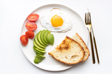 Fried egg, avocado, tomatoes and toasts on the plate. Top view on healthy breakfast.