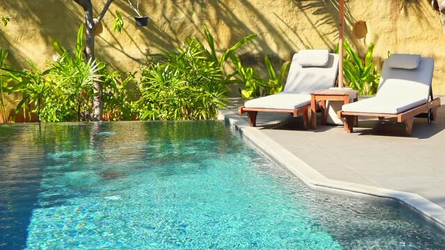 Luxury lounge area for a couple rest with two deck chairs and umbrella next to the swimming pool surrounded with green plants background