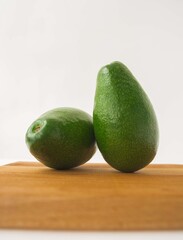 2 green ripe avocados on a wooden board