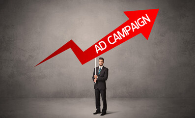 Fototapeta premium Young business person in casual holding road sign with AD CAMPAIGN inscription, business direction concept