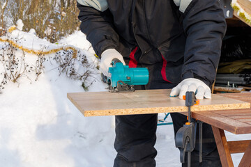 A male worker cuts a wooden panel attached to a workbench with clamps using a circular disc on a battery.