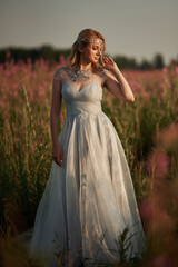 Fototapeta na wymiar Romantic blonde woman running in a wonderful flower field. Warm sunset colors. Blue dress. Soft colors.