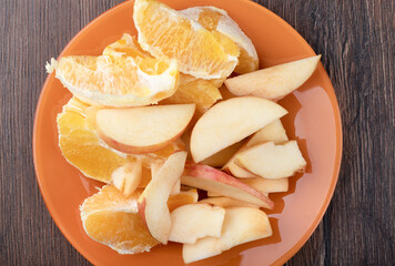 Top view of an orange plate with sliced apples and oranges.